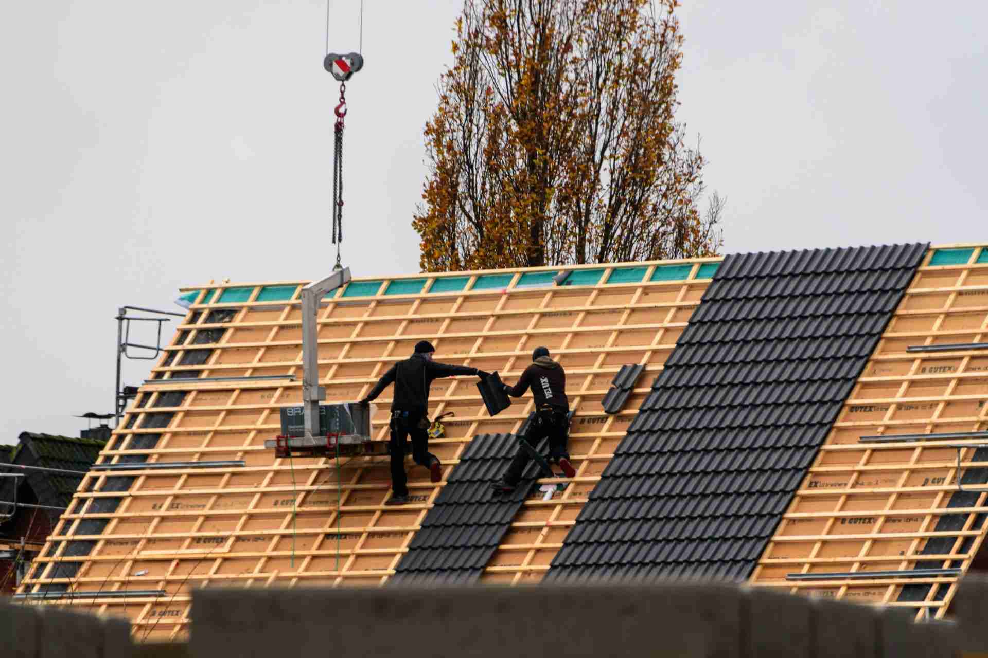 Bauarbeiter verlegen Dachziegel auf einem Neubau.